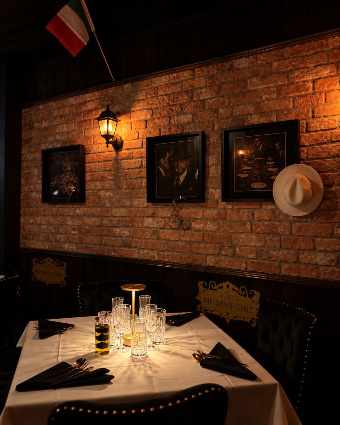Corner table under an Italian flag and a white fedora, brass plaque reading The Soprano Table