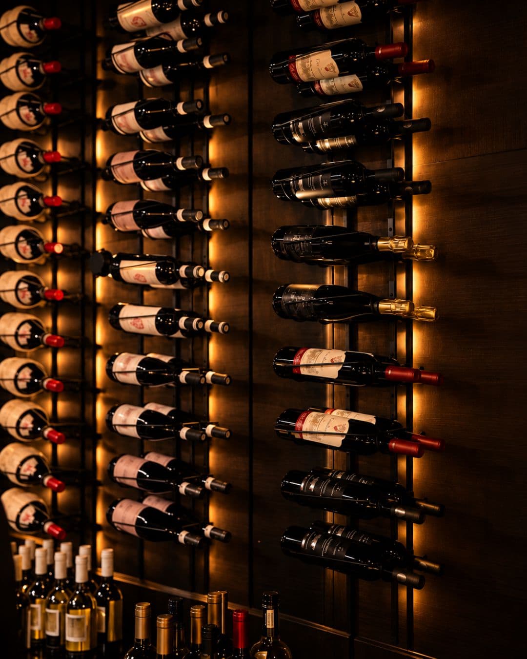 The wine wall: bottles racked on dark wood, lit from behind