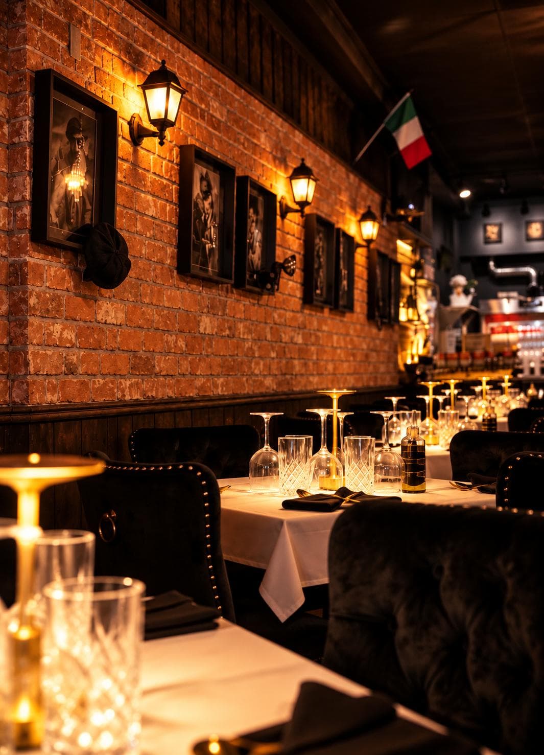 Lanterns and framed black-and-white portraits along the brick wall, above tables set with crystal glasses and brass lamps