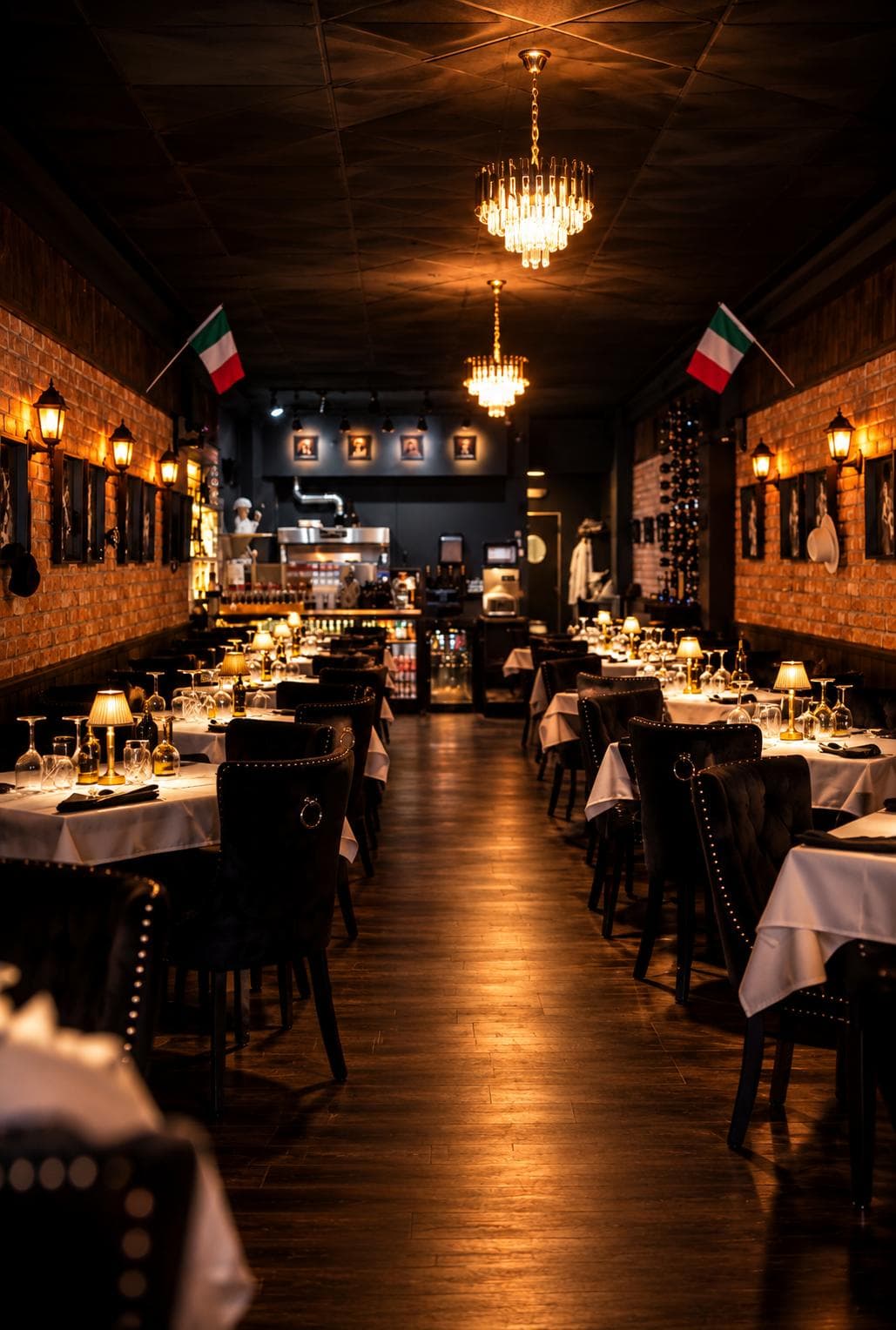 The dining room from the front: two crystal chandeliers, Italian flags on the brick walls, tables laid in white down both sides to the open kitchen