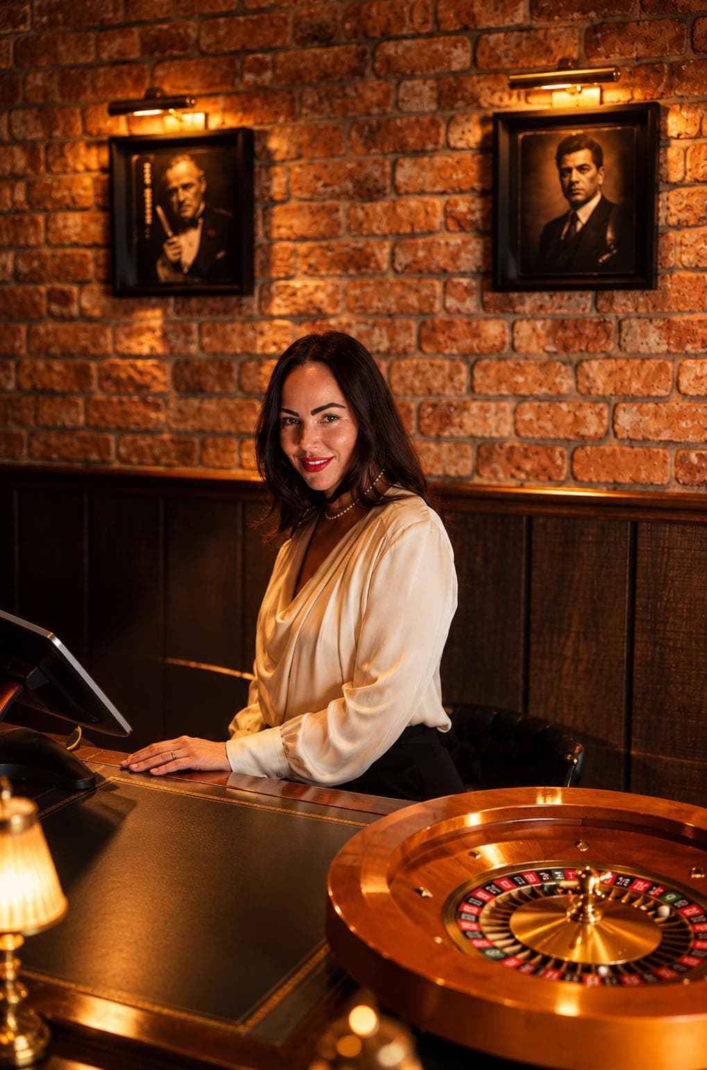 The host smiling at the front desk, a roulette wheel at the end of the counter and portraits on the brick wall behind